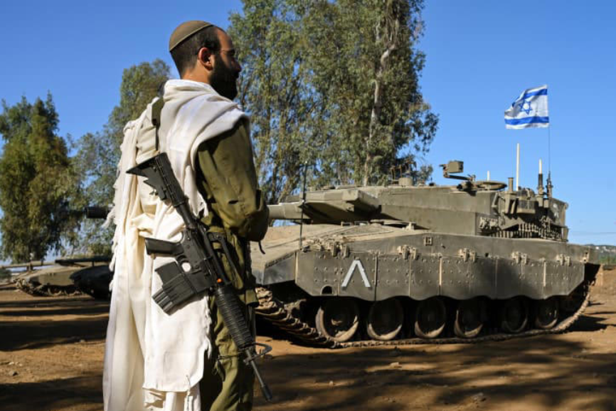 An Israeli soldier with a prayer shawl seen during a morning prayer near his tank near the border with Lebanon, northern Israel, October 25, 2023